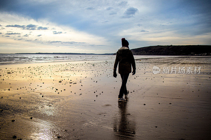 在一个寒冷的春天的早晨，英国威尔士南岸彭布罗克郡，一个孤独的女人走在彭丁Sands Carmarthen Bay的一个孤立的海滩上
